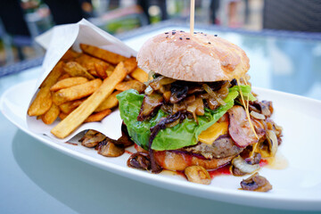 Appetizing juicy meat burgers, potato chips and vegetable in restaurant. French fries, hamburger or cheeseburger and sauces on plate with copy space. Fast food menu.