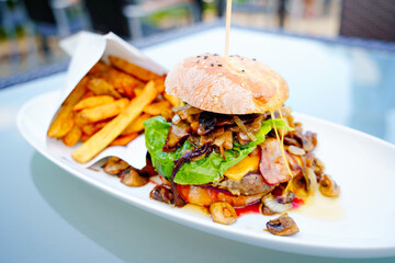 Appetizing juicy meat burgers, potato chips and vegetable in restaurant. French fries, hamburger or cheeseburger and sauces on plate with copy space. Fast food menu.