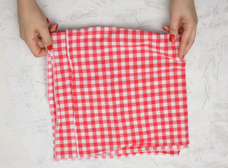two female hands hold a crumpled white-red checkered textile kitchen napkin on a white table