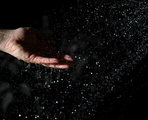 Fototapeta na wymiar female hand and flying drops of water on a black background