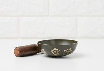Tibetan singing copper bowl with a wooden clapper on a white wooden table, objects for meditation...