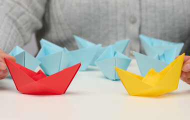 Naklejka premium female hands hold red and yellow paper boats on a white table. Confrontation, follow a strong leader, dailog