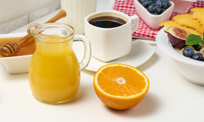 half a ripe orange and freshly squeezed juice in a glass transparent decanter, a cup of coffee, honey and oatmeal on a white table.