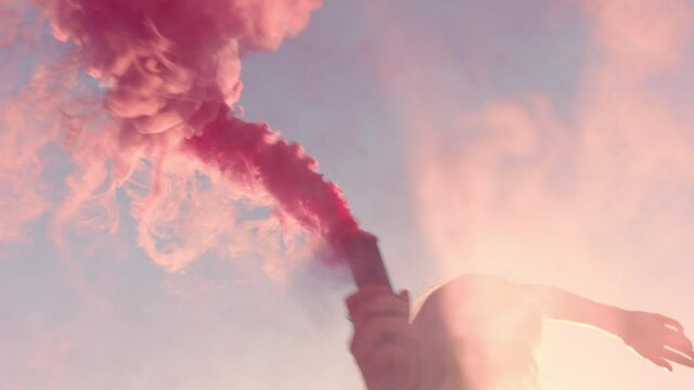 beautiful woman waving pink smoke grenade dancing on beach at sunrise celebrating creative freedom with playful dance movement