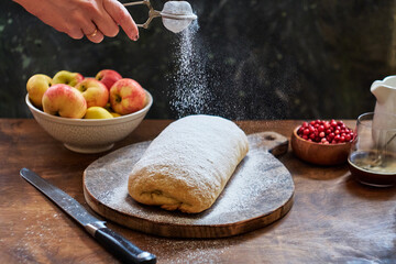 Strudel with apples and cranberries. Icing sugar, coffee, berries. Wooden background, side view. Dust the strudel with icing sugar.