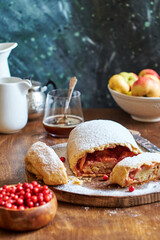Strudel with apples and cranberries. Icing sugar, coffee, berries. Wooden background, side view. 