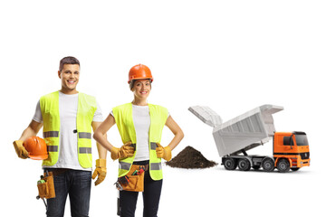 Male and female construction workers wearing hardhats at a site with a dump truck