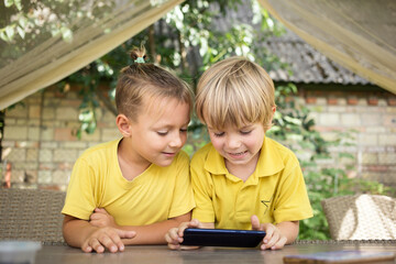 Cute 5-year-old boys, brothers in yellow T-shirts, are looking with interest at phone screen in front of them. modern children, digital age, curiosity, online education for children, games on gadgets