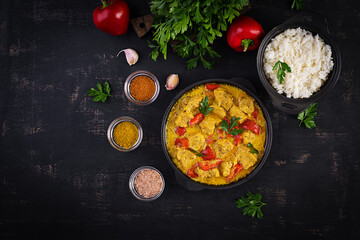 Traditional Indian curry chicken masala. Indian chicken curry with sweet peppers and  rice in bowl, spices, dark background. Traditional Indian dish. Top view, flat lay