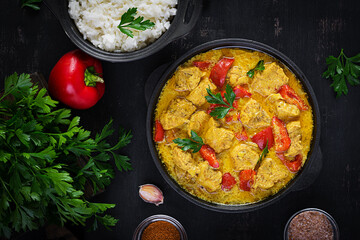 Traditional Indian curry chicken masala. Indian chicken curry with sweet peppers and  rice in bowl, spices, dark background. Traditional Indian dish. Top view, flat lay