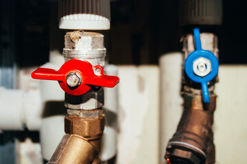 Two valves on plastic and metal pipes with hot and cold water. Open blue and closed red switches....
