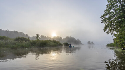 Fototapeta na wymiar Early morning. Fog on the river. Beautiful sunrise in the summer by the river. Mystical morning on the river. A man floats in a boat against the background of dawn.