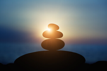 Rock pebble pyramid silhouette at sunset light, zen stones on sea beach, meditation, spa, harmony,...