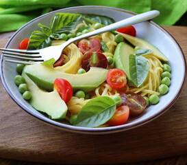 Pasta salad with green peas, avocado, cherry tomatoes and basil on rustic wooden background. Top view