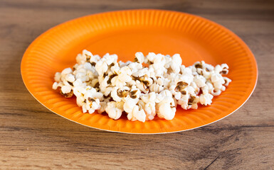popcorn on an orange paper plate on a wooden table