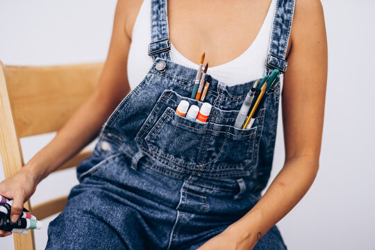 Brushes and paints in the pocket of denim overalls