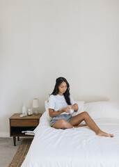 Obraz na płótnie Canvas Young Filipino woman sitting on bed drinking coffee