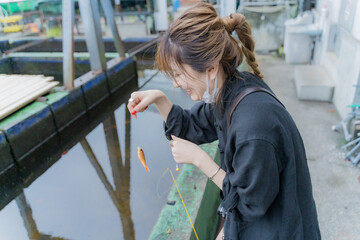 釣れた金魚の針を外す女性