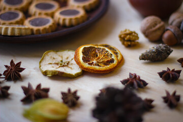Fall season photo. Dried slices of orange, apple, acorns, physalis, and in the background there is a plate of cookies