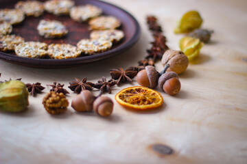 Fall season photo. Dried slices of orange, apple, acorns, physalis, and in the background there is a plate of cookies