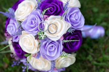 Wedding bouquet of satin roses and gold rings. Artificial or fake pink, violet and purple rose in bridal flower.
