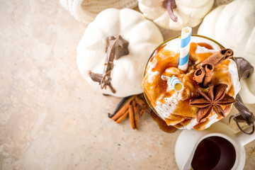 Pumpkin spice latte or milkshake,traditional autumn hot drink with anise, cinnamon, caramel topping, on warm colored background with small decorative pumpkins and cozy sweater, 