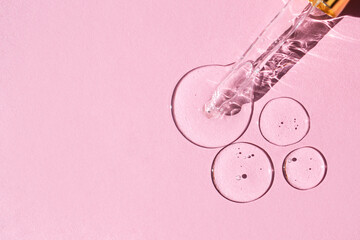 Transparent drops of hyaluronic acid and glass pipette on pink background.  Glass pipette with a drop of face serum with air bubbles. Top view, place for text.  - obrazy, fototapety, plakaty