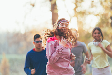 Red hair female with group of young friends enjoys an invigorating jog in the park during a crisp autumn afternoon, surrounded by vibrant foliage.	