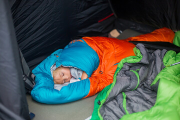 Cute toddler blond child, boy, sleeping in sleeping bag in a tent on a vacation in Norway, wild...