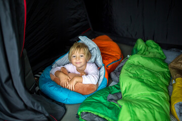 Cute toddler blond child, boy, sleeping in sleeping bag in a tent on a vacation in Norway, wild...