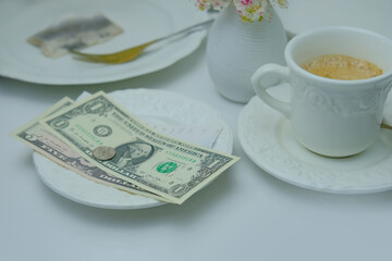 close-up on white plate with American dollars bills and coins, selective focus, cup of coffee, dishes with food, lunch concept in restaurant, cafe, tip money concept, change of waiter