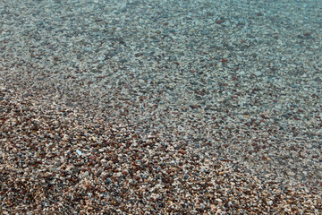The beach is made of pebbles, the seashore, small colored pebbles in the water. Background, copy space.