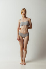 Fototapeta premium Portrait of young adorable woman in lingerie isolated over gray studio background. Natural beauty concept. Authenticity, natural beauty