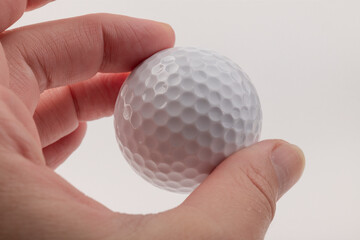 female hand holding golf ball on light background. The white color of plastic ball is popular in the game
