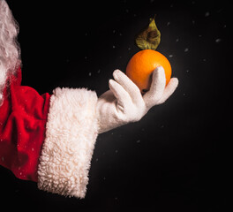 Fresh orange in Santa's hand. Fragment close-up on a black background.