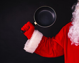 Santa Claus hand holding a frying pan on a black background, cooking festive dinner.
