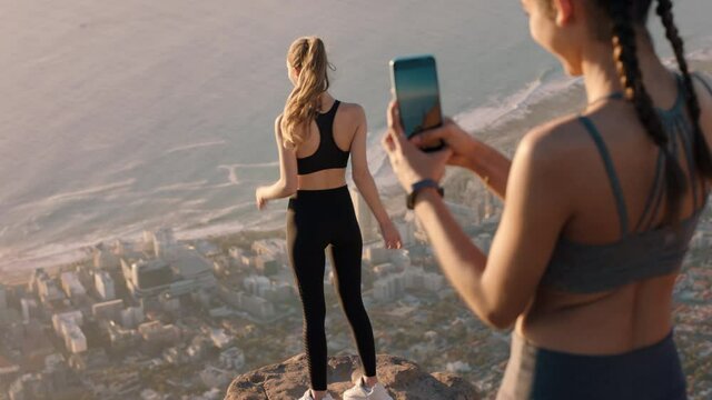 girl friends taking photo on mountain top using smartphone camera beautiful young woman posing for friend with mobile phone sharing hiking adventure on social media