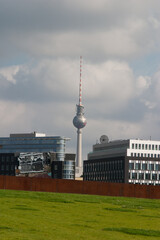 Obraz premium The iconic TV tower of Berlin seen amongst modern buildings and a section iron wall