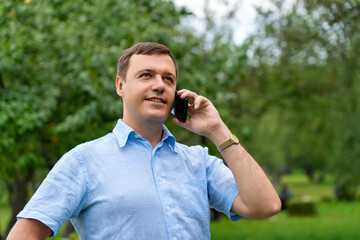 Young caucasian man talking on smartphone at summer park. Happy millennial business man outdoors in conversation at mobile phone.