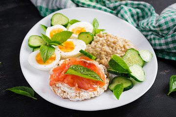 Breakfast oatmeal porridge with boiled eggs, salmon sandwich and cucumbers salad. Healthy food. Lunch.