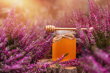heather honey in a jar and a wooden honey spoon among the heathers - obrazy, fototapety, plakaty
