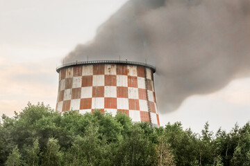 Dirty gray smoke pollutes the amospheric and nature standing out from the cooling tower of an industrial enterprise