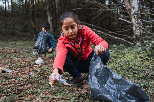 Ethnic children collecting garbage from land in forest