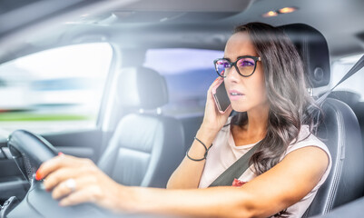 Fototapeta na wymiar Woman in glasses driving a car calls on a cell phone, holding steering wheel with only one hand