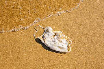 Used face mask on the sand. Covid-19 protection. Environment pollution concept.