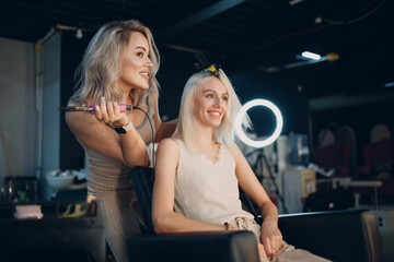 Hairdresser female making hair extensions to young woman with blonde hair in beauty salon. Professional hair extension