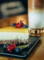 Close Up Photo of a Iced Coffee and Slice of Cake on a Table. 
Your order is ready: sugar free healthy dessert with fruits and nuts and glass of ice latte coffee on the bar counter.