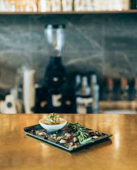A Healthy Protein Ball with Pistachios on a Black Plate in a Restaurant. 
Your order is ready: sugar free energy ball rolled in sliced pistachio nuts served on a black plate on a golden bar counter.