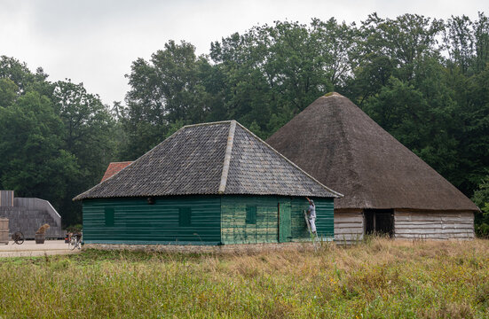 Genk, Belgium - August 11, 2021: Domein Bokrijk. 2 barns, one is painted and has tile roof, while the other. the biggest has thick straw roof. Green meadow in front, darker green foliage in back.
