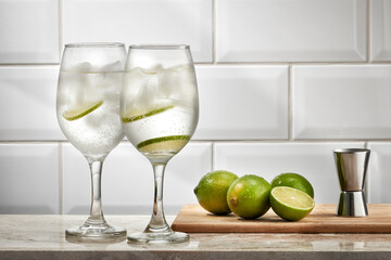 Copos com água, fatias de limão e gelo, sobre bancada com limões ao lado